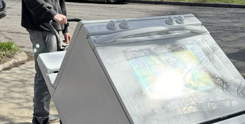 A person standing next to a vintage white washing machine outdoors, with the lid open and a map visible through the glass.